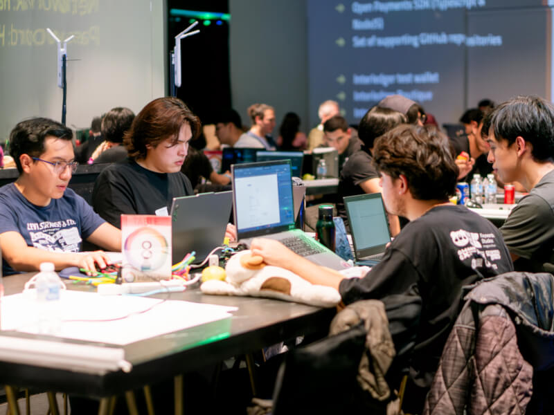 Team of developers working together on laptops at a table during the Interledger Hackathon 2025.