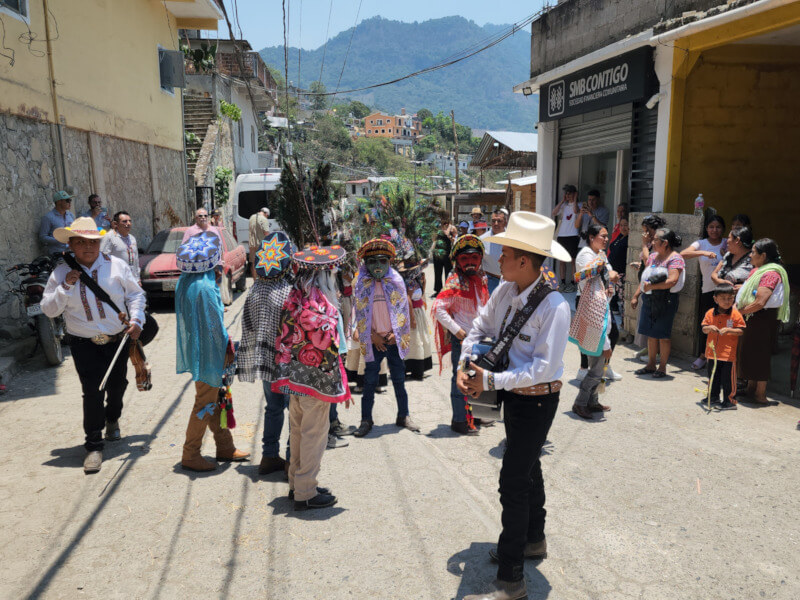 Thumbnail image of a festive street in rural Mexico, showing people in traditional costumes and masks dancing, with a young man playing guitar in the center.
